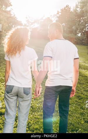 Vista posteriore del giovane redhead matura per mano e camminare insieme in posizione di parcheggio Foto Stock