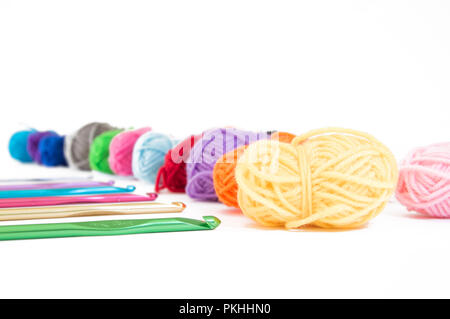 Una fila di filato colorato con aghi a crochet schierati al loro fianco su un tasto alto sullo sfondo. Foto Stock