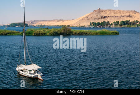Tradizionale feluca e barca a vela e la vista della collina tomba del profeta musulmano, Qubbet el Hawa sulla sabbia cliff, Fiume Nilo, Aswan, Egitto, Africa Foto Stock
