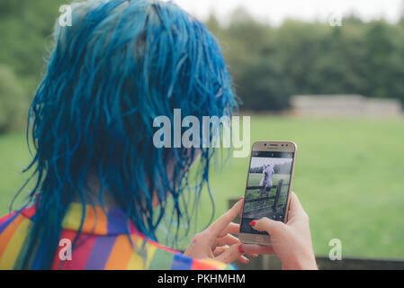 Un blu donna dai capelli, indossando un Gay Pride come top, scatta una foto di una casa sul suo cellulare / Telefono cellulare Foto Stock