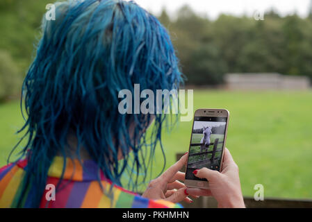 Un blu donna dai capelli, indossando un Gay Pride come top, scatta una foto di una casa sul suo cellulare / Telefono cellulare Foto Stock