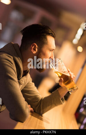 Un bel giovane hipster uomo a bere una birra al bar. Foto Stock