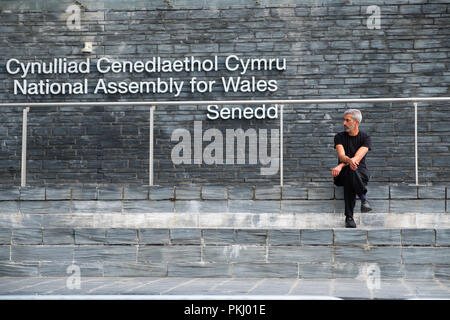 Welsh governo: un uomo seduto sui gradini al di fuori dell'ardesia-placcati Assemblea nazionale del Galles edificio, esterno, Cardiff Wales UK Foto Stock