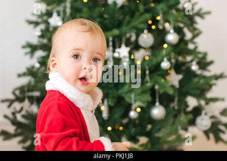 Little Boy in Santa costume in piedi vicino all albero di Natale Foto Stock