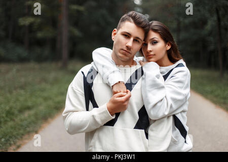 Giovane e bella coppia elegante in bianco identiche maglioni abbracciando nel bosco Foto Stock