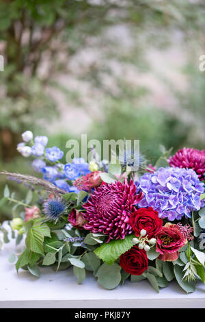 Allungate la disposizione floreale in metallo vintage vaso. Impostazione tabella. Colore blu e rosso. Splendidi bouquet di fiori diversi. Park sullo sfondo Foto Stock