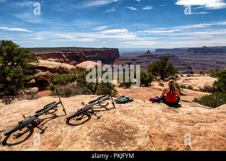 Una donna si ferma per una pausa mentre in sella ad una mountain bike lungo un sentiero in Dead Horse Point State Park, Utah, Stati Uniti d'America. Foto Stock