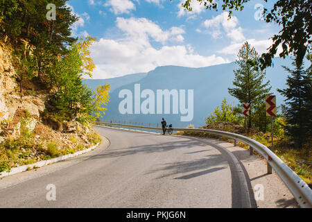 Un uomo si erge accanto a una bicicletta sul lastricato della strada di montagna. In estate le montagne della Bulgaria Foto Stock