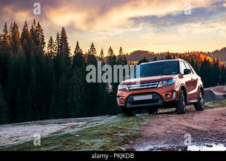 Orange 4wd suv parcheggiato in montagna a sunrise. bellissimo paesaggio autunnale con strada di ghiaia attraverso foreste di abete rosso. viaggia in Europa dal concetto di automobile Foto Stock