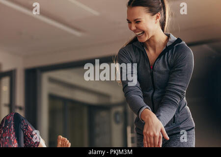 Femmina guida trainer donna durante il pilates formazione presso una palestra. Femmina istruttore pilates ridere mentre la formazione della donna in una palestra. Foto Stock