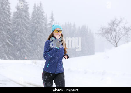 Giovane donna in esecuzione sulla strada di montagna in inverno Foto Stock