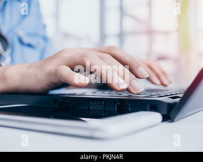 Chiudere fino a mani digitando su nero computer portatile e la tastiera del telefono cellulare sul tavolo bianco in bianco cafe sfondo con copia spazio. Foto Stock