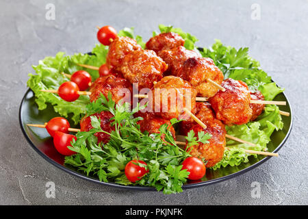 Le polpette di carne arrosto su spiedini con pomodori freschi su un letto di foglie di lattuga, vista orizzontale da abov Foto Stock