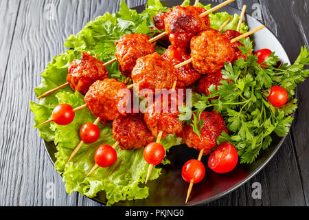 Le polpette di carne su spiedini con pomodori freschi su un letto di verdure su una piastra nera, street food, vista orizzontale dal di sopra, close-up Foto Stock