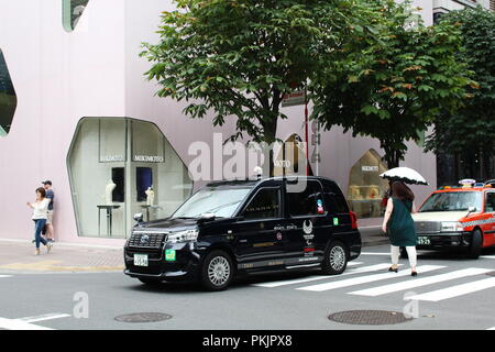 Una Toyota JPN Taxi di Tokyo Olimpiadi logo 2020 su di esso andando oltre un crosswalk nella parte anteriore della Toyo Ito-progettato Mikimoto Ginza 2 store in Tokyo. Foto Stock