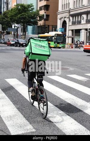 Un Uber mangia un addetto alle consegne di biciclette attraversando un grande incrocio (4 Chome) nel quartiere Ginza di Tokyo. Il grande magazzino Wako è in background. Foto Stock