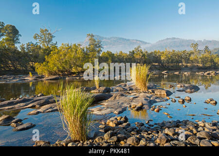 Incredibile paesaggio australiano con rock disseminata blu delle acque del fiume Mann orlate da foreste a piedi di intervalli sotto il cielo blu di mattina presto in NSW Foto Stock