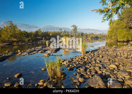 Incredibile paesaggio australiano con rock disseminata blu delle acque del fiume Mann orlate da foreste a piedi di intervalli sotto il cielo blu di mattina presto in NSW Foto Stock