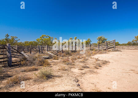 Arido entroterra australiano di paesaggio con decadendo vecchi cantieri del bestiame in pianure intonacato con bassa vegetazione sotto il cielo blu durante la siccità nel Queensland Foto Stock