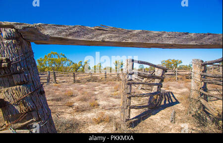 Arido entroterra australiano di paesaggio con decadendo vecchi cantieri del bestiame in pianure intonacato con bassa vegetazione sotto il cielo blu durante la siccità nel Queensland Foto Stock