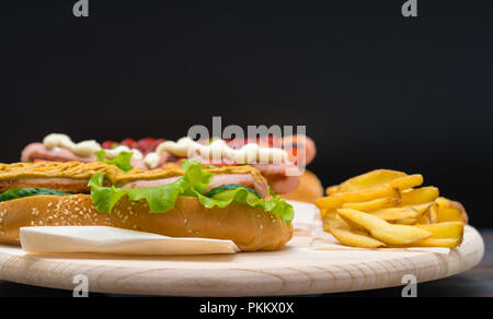 Hot Dog e rabboccato con senape piccante e servita con croccante di incendi francese su un rustico in legno scheda sopra uno sfondo scuro con spazio di copia Foto Stock