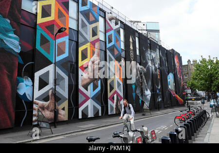 Un hipster escursioni in bicicletta su una bici passato un grande arte di strada pittura murale a New Inn Yard Shoreditch vicino a Hackney in East London REGNO UNITO KATHY DEWITT Foto Stock