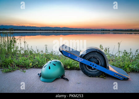 Fort Collins, CO, Stati Uniti d'America - 11 agosto 2018: OneWheel skateboard elettrico con un casco su un lago mal contro il cielo al tramonto. Foto Stock