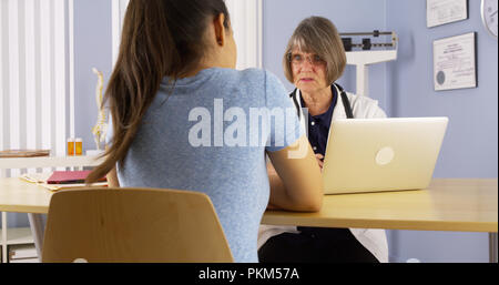 Senior medico prendendo appunti sul computer portatile e parlare per il paziente Foto Stock