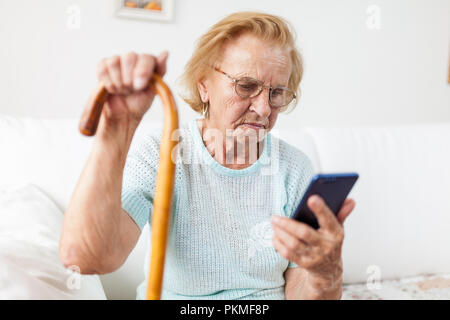 Donna anziana con gli occhiali e la canna da zucchero usando un telefono cellulare Foto Stock