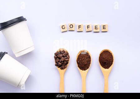 Cucchiai di legno riempito di caffè in grani frantumati e caffè macinato , carta tazza di caffè e di parola su sfondo bianco Foto Stock