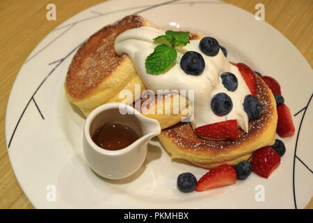 Souffle deliziosi pancake con sciroppo d'acero, panna montata e mescolare bacche servita su piastra bianca Foto Stock