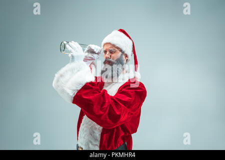 Funny ragazzo con cappello di Natale in posa in studio. Nuovo anno di vacanza. Natale, X-mas, inverno, doni concetto. Uomo che indossa Santa Claus costume sul grigio. Copia dello spazio. Winter Sales. Foto Stock