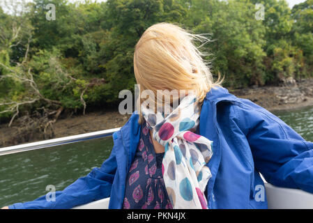 Donna su una barca con i suoi capelli biondi soffiata attraverso il suo viso dal vento e non riesce a vedere. Foto Stock
