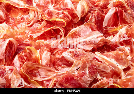 Stuzzicanti fette di prosciutto iberico in primo piano come una texture. La carne cruda che diventa un articolo di alta cucina gastronomica e di lusso, attraverso una proc Foto Stock
