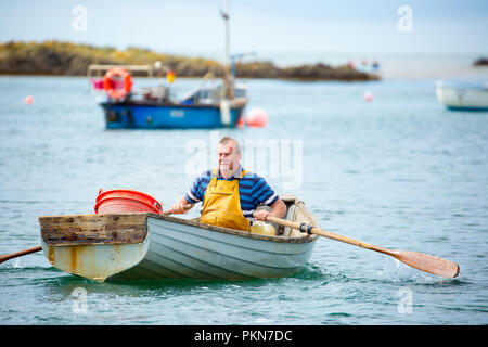 Tiro d'azione del pescatore britannico tradizionale isolato in barca a remi, che si canala verso il mare. Foto Stock