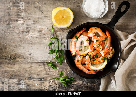 Grigliata di gamberi, prezzemolo e limone in padella di ferro sul tavolo di legno. Vista dall'alto. Copyspace Foto Stock