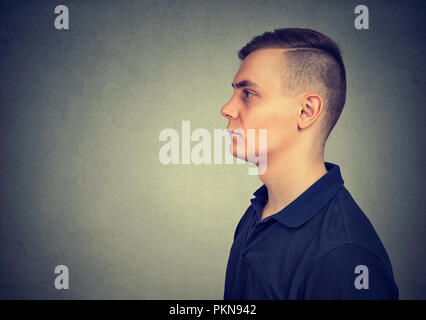 Profilo del giovane uomo bello in t-shirt casual cercando seriamente di distanza su sfondo grigio Foto Stock