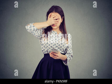 Giovane donna fare errore mentre si utilizza lo smartphone e guardando triste su sfondo grigio Foto Stock