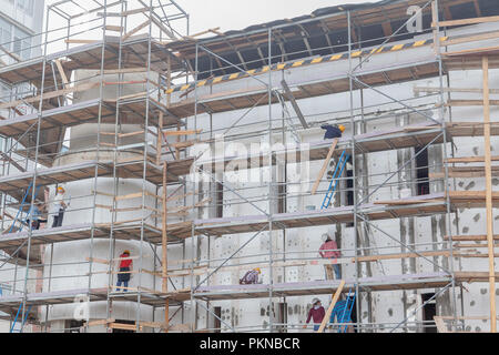 Costruzione professionale dei lavoratori sul patibolo ascensore parete isolata facciata con lana minerale. conciatetti indossare l'imbragatura di sicurezza la parete isolante fac Foto Stock