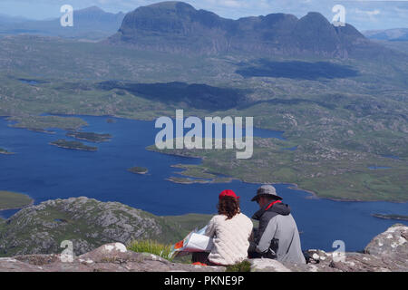 Un giovane di età in anni cinquanta seduto sulla montagna, Stac Pollaidh guardando attraverso il paese con Suilven mountain in background. Entrambi indossare cappelli. Foto Stock
