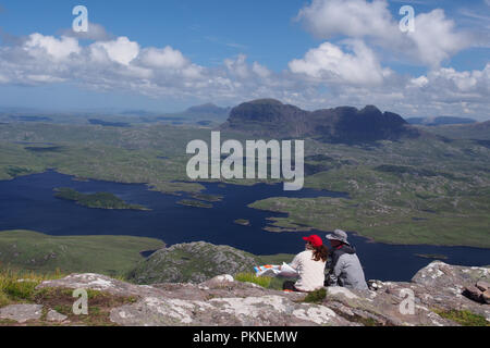 Un giovane di età in anni cinquanta seduto sulla montagna, Stac Pollaidh guardando attraverso il paese con Suilven mountain in background. Entrambi indossare cappelli. Foto Stock