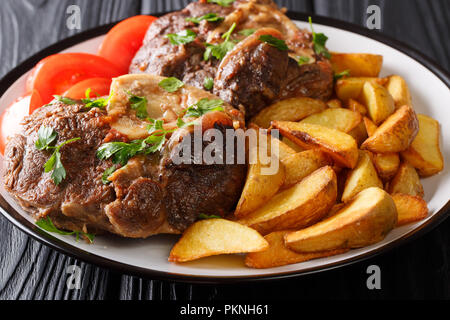 Bistecca piccante ossobuco con patate fritte cunei e pomodori close-up su una piastra su un piano orizzontale. Foto Stock