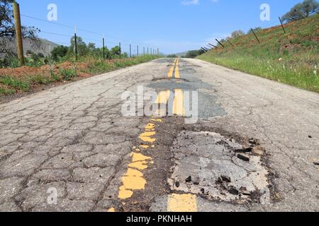 Strada danneggiata di Yokohl Drive in California, Stati Uniti d'America - Asfalto Screpolato asfalto con buche e patch. Foto Stock