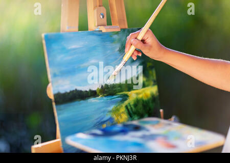 Giovane donna graziosa artista disegna dipinge un quadro di un lago su open plain air all'aperto Foto Stock