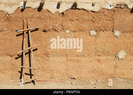 Sfondo di fango parete testurizzata con scaletta fatti a mano appoggiata su di un adobe nel deserto del Sahara in Marocco Foto Stock