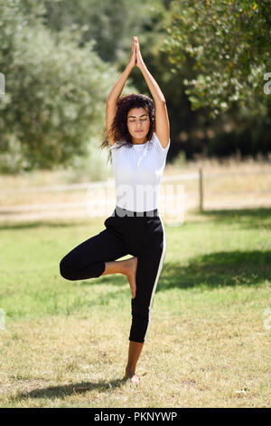 Giovane donna araba fare yoga in natura. Nord femmina africana indossando indumenti sportivi albero facendo la figura nel parco urbano. Foto Stock