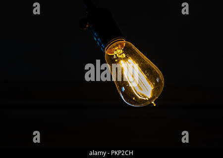 Alla moda di lampadina appesa contro uno sfondo nero. Foto Stock