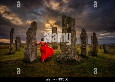 Donna in abito rosso a Callanish pietre nella luce del tramonto, Lewis, Scozia Foto Stock