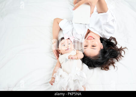 Una donna con un bambino facendo un selfie sdraiato sul pavimento in legno Foto Stock