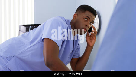 Americano africano medico maschio sul cellulare parlando a un collega e uso del computer Foto Stock